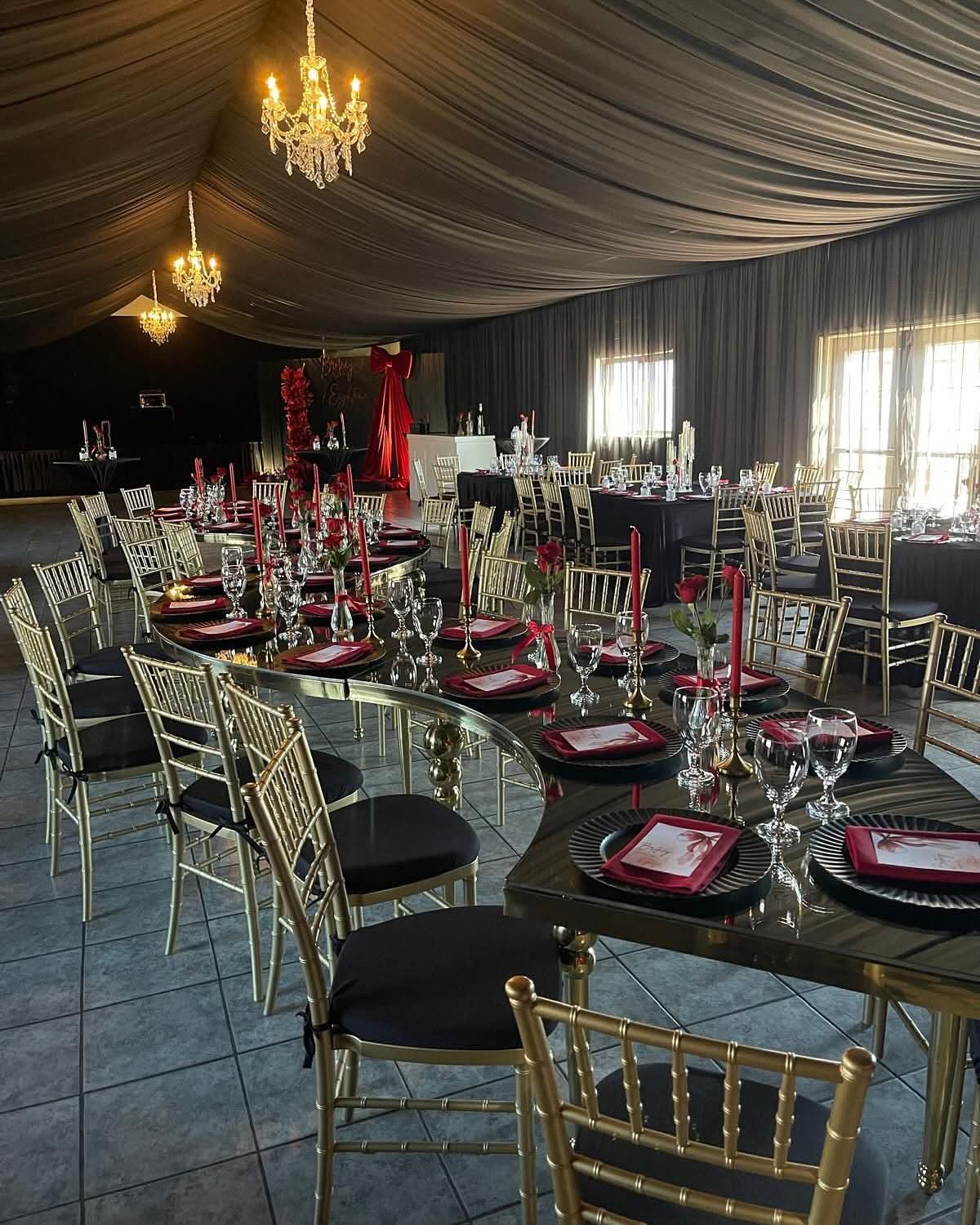 Montaje elegante con mesas, sillas doradas y decoración en tonos rojo y negro